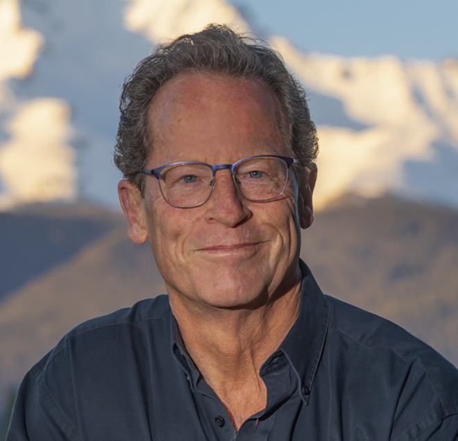 Gavin Taylor headshot in front of mountians and blue, cloudy sky