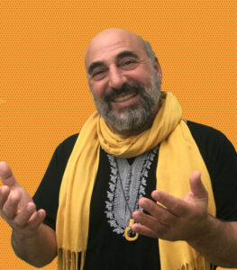 Dror Sinai from Rhythm Fusion, smiling with hands open and facing up with a yellow scarf and gold background