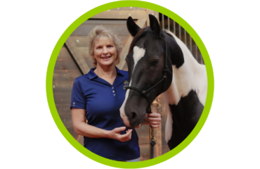 photo of April Love smiling with a blue shirt, holding the reigns of a black and white horse