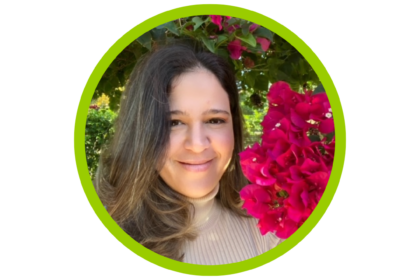 Elisa Calosso in brown shirt with hair to one side, smiling with no teeth with a background of pink flower tree