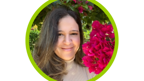 Elisa Calosso in brown shirt with hair to one side, smiling with no teeth with a background of pink flower tree